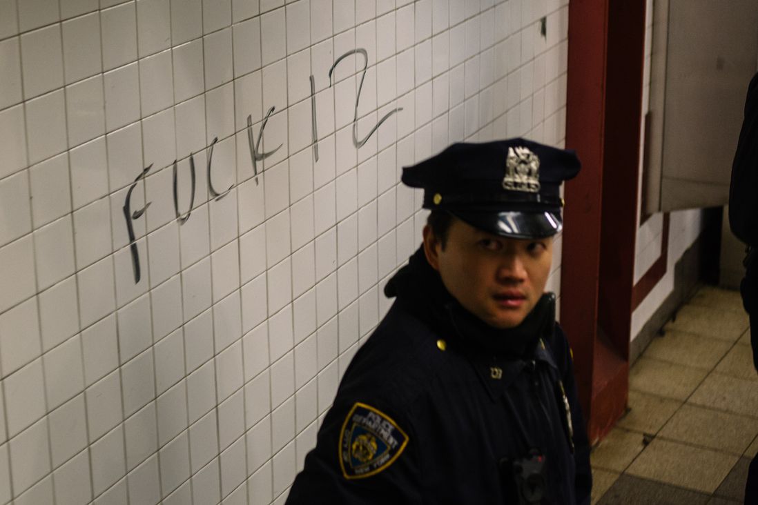 A police officer stands next to graffiti on the subway.